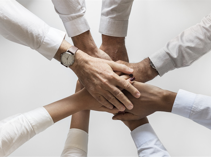close up of arms and hands, arms in a circle with all their hands on top of one another in the center