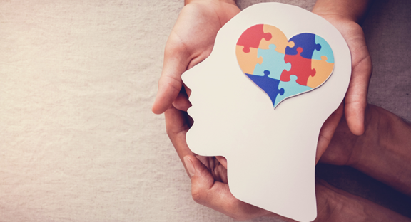 close up of 2 people holding hands and a paper cutout of a silhouetted person's head and a heart made of puzzle pieces where their brain is located