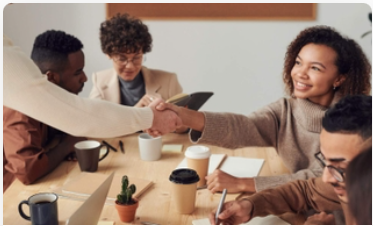 people sitting at conference table, some taking notes, some in conversation and two shaking hands