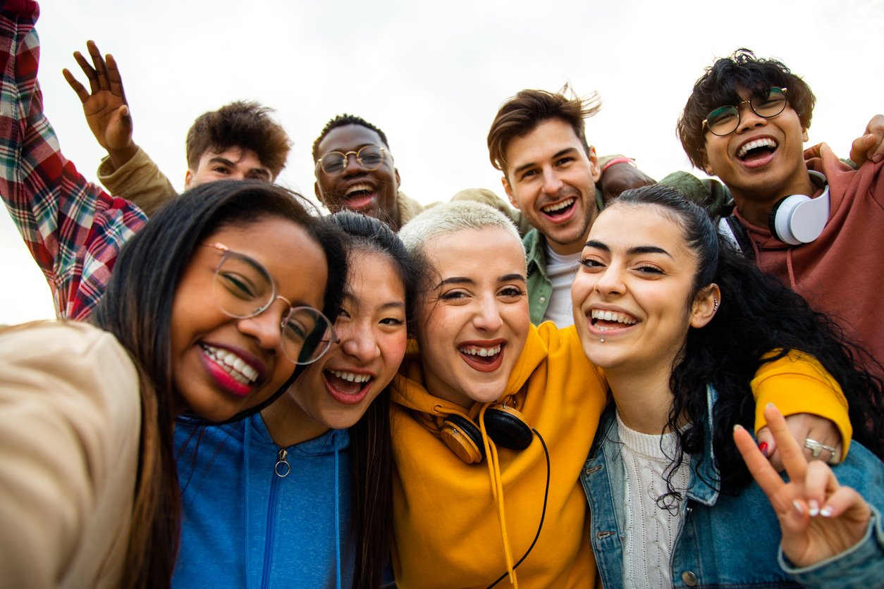 group of smiling teens with arm around each other and some waving in the air