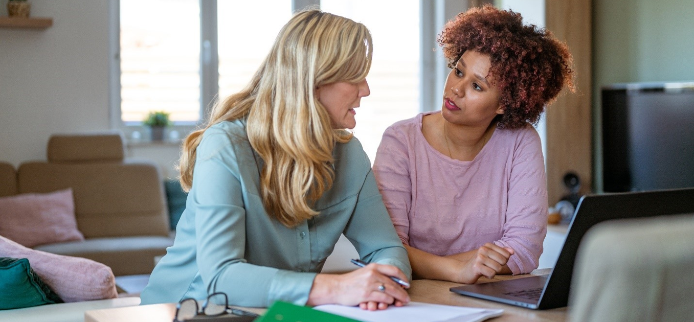 Two woman sitting at a desk with a laptop and papers in discussion
