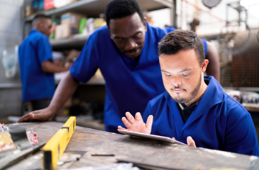 man with down syndrome on ipad with another man looking over his shoulder at the ipad in a work environment