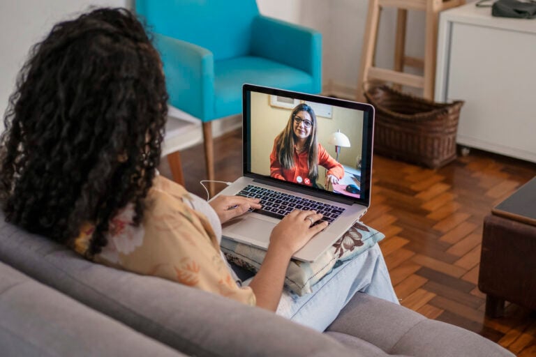 woman with laptop sitting on living room couch while on a video conference with a doctor