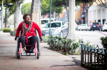 Smiling Black woman wheeling herself down a sidewalk in a wheelchair