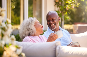 An older Black couple enjoying a cup of coffee while sitting on an outdoor couch