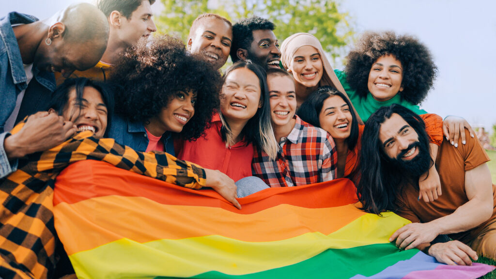 Happy diverse people holding lgbt rainbow flag outdoors - Diversity concept - Soft focus on Asian young woman face