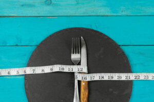 Fork and Knife tied together with a measuring tape on a black circle napkin against an aqua painted table.